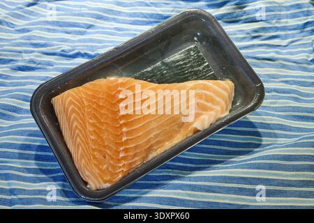 A piece of raw salmon in plastic packaging on blue stripped lines Stock Photo
