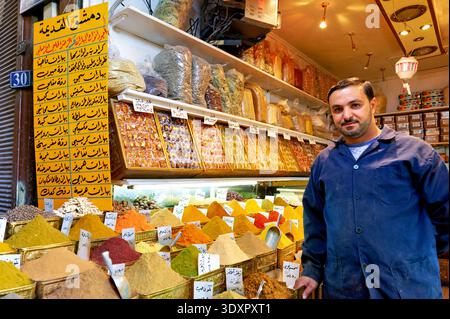 In Al Silah Souq, a vendor stands near a display of various spices in Damascus. Customers browse the colorful selection of spices. Stock Photo