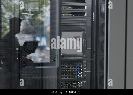 Data center server racks and monitoring equipment reflected in glass with technician working in modern facility Stock Photo