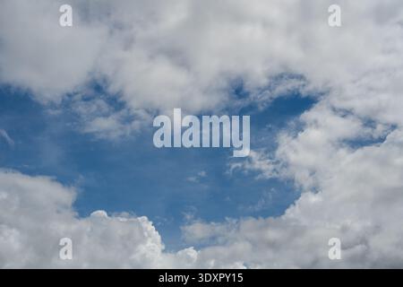 Blue sky visible through an opening in thick white clouds Stock Photo