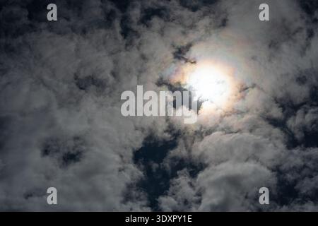 Sun glowing through dark grey clouds with slight iridescence Stock Photo