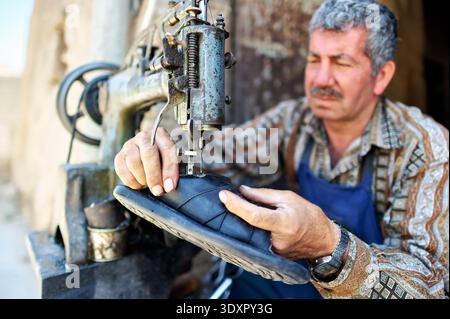 A man repairs a shoe using a sewing machine in the busy souq of Aleppo, Syria. The scene shows the craft of shoemaking. Stock Photo