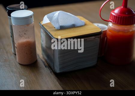Tissue box spice shaker and red sauce bottle on a wooden table Stock Photo