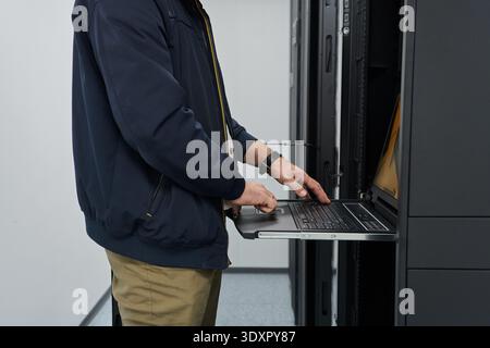 IT technician working on laptop in server rack inside data center performing network maintenance and hardware monitoring Stock Photo