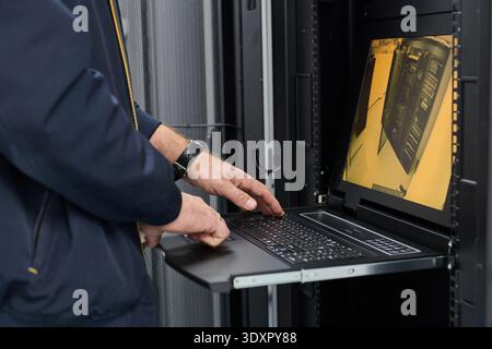 IT technician working on rack server console laptop in a data center server room monitoring equipment Stock Photo
