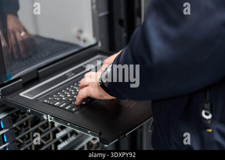 IT technician typing on a rack console laptop in a data center server room during maintenance Stock Photo