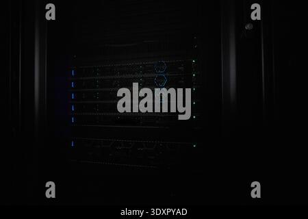 Server rack with illuminated network hardware and blinking LEDs in a dark data center Stock Photo