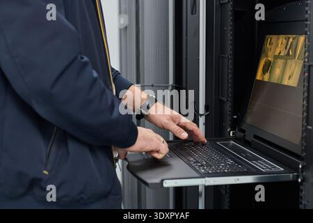 Data center technician monitoring servers and surveillance on a rack-mounted console while troubleshooting systems Stock Photo