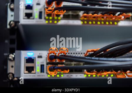 Close-up of network server rack with fiber optic cables and illuminated ports in data center Stock Photo