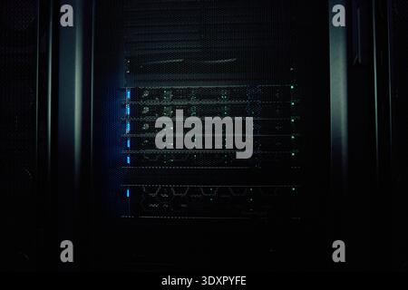 Dark server rack with glowing network equipment and status lights in a data center cabinet Stock Photo
