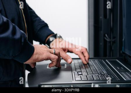 IT technician typing on laptop console in a data center server rack performing maintenance Stock Photo