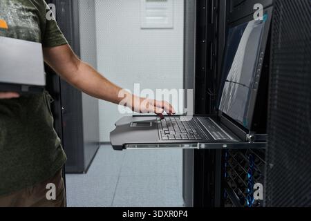 IT technician working on rack-mounted console laptop in a data center server room Stock Photo