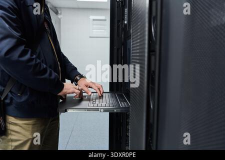IT technician maintaining server rack with pull-out console laptop in a data center Stock Photo