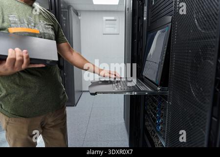 Data center technician using rack console laptop for server maintenance and IT network troubleshooting Stock Photo