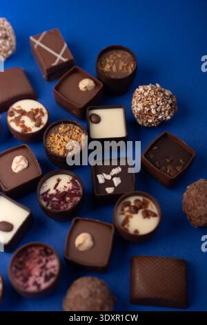 assorted artisanal chocolate bonbons and truffles artfully arranged on a vivid cobalt-blue background, showcasing varied shapes, nut toppings, creamy Stock Photo