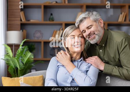 Senior couple embracing and smiling in their living room, representing enduring love, happiness, and companionship in retirement life and a strong relationship Stock Photo