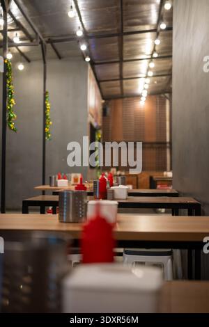 Empty wooden tables with red squeeze bottles under string lights Stock Photo