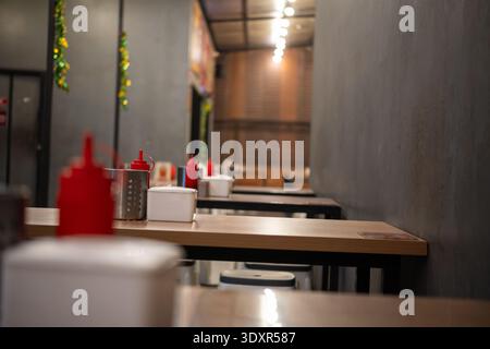 Empty wooden tables with red squeeze bottles in a dim indoor space Stock Photo