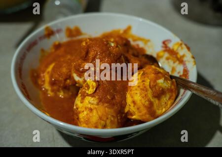 Boiled eggs covered in red chili sauce in a white bowl Stock Photo