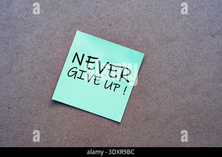 Handwritten "Never Give Up!" on a green sticky note. Motivational concept for resilience, persistence, and overcoming challenges on a wooden backgroun Stock Photo