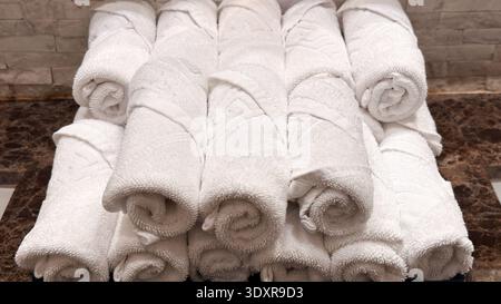 Soft and inviting rolled white towels on a luxurious brown marble countertop in a modern bathroom setting Stock Photo