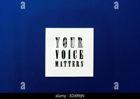 White square note with "YOUR VOICE MATTERS" bold text centered on a dark blue textured background, representing empowerment, democracy, freedom. Stock Photo