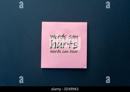 Pink sticky note with "Words can hurts, words can heal" text on a dark blue background, highlighting the power of language, mental health awarenes. Stock Photo