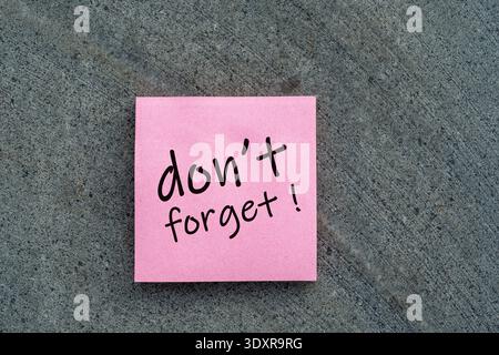Pink sticky note with "Don't Forget!" handwritten message on a grey stone background. Concept for reminders, task management, and personal appointment Stock Photo