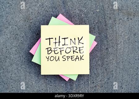 Yellow sticky note with "Think Before You Speak" message on colorful paper layers and stone background, representing mindfulness, communication skill Stock Photo