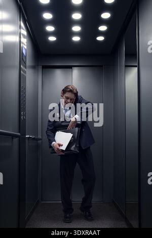 Young businessman searching documents inside briefcase while standing in office elevator. Stock Photo