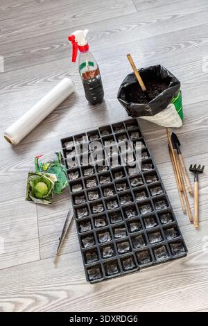 Vertical shot of a seed starting kit with a tray, soil, spray bottle, plastic film, seed packets and mini gardening tools on a light wooden background Stock Photo