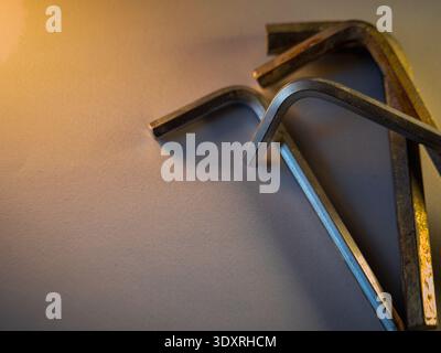 Metal hex keys rest on a cool gray surface. Warm light casts soft shadows around the tools. Each key shows signs of frequent use. Tools lie casually, Stock Photo