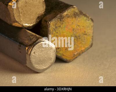 Hexagonal bolts rest side by side on textured surface. One bolt gleams with fresh, metallic finish. Another shows signs of rust and wear. Close-up hig Stock Photo