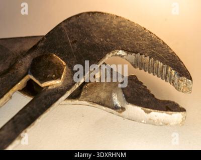 Old pipe wrench rests on a plain surface. Metal shows wear, rust, and heavy use. Jaw teeth grip tightly, showing strength. Tool's handle holds a hex b Stock Photo