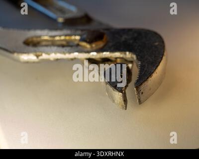 Worn wrench rests on soft, neutral surface. Metal shows signs of heavy use and age. Bright light highlights texture and wear. Close-up emphasizes tool Stock Photo