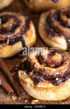 Fresh baked cinnamon glazed rolls  with cinnamon sticks on wooden table closeup Stock Photo