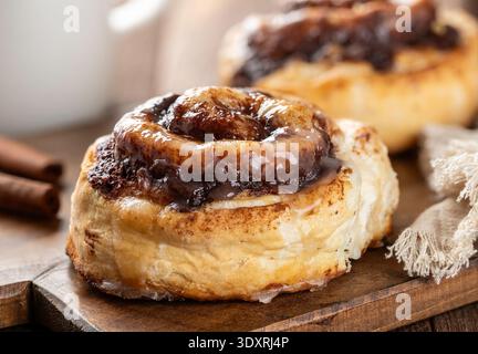 Fresh baked cinnamon glazed rolls  with cinnamon sticks on wooden board closeup and coffee mug in background Stock Photo