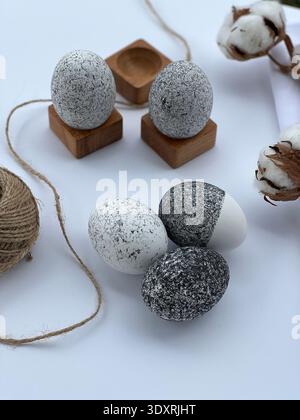 Minimalist Easter still life with decorative stone eggs, cotton branch and wooden holders on white background, natural Scandinavian style decor. Stock Photo