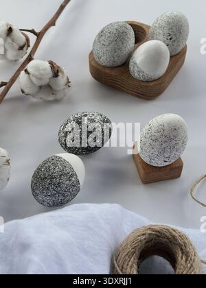 Minimalist Easter still life with decorative stone eggs, cotton branch and wooden holders on white background, natural Scandinavian style decor. Stock Photo