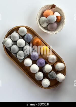 Minimalist Easter still life with colorful decorative eggs arranged on wooden tray and bowl on white background, modern Scandinavian style Stock Photo