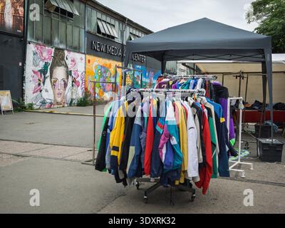 Clothing Rack Displayed Outside Building with New Media Center Sign and Vibrant Street Mural in Berlin. Stock Photo