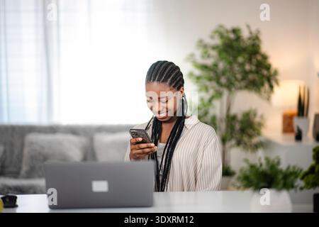 Young black woman smiling using phone at home Stock Photo