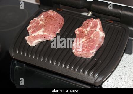 Two fresh raw pork steaks placed on an electric grill pan ready for cooking in a home kitchen, preparing meat for a grilled meal Stock Photo