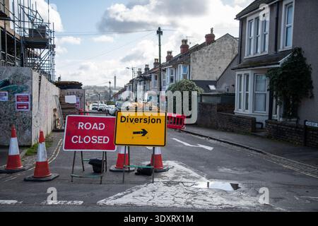 Red Road Closed sign beside yellow Diversion arrow sign on a roadside. Traffic management concept, transport disruption and temporary direction signag Stock Photo
