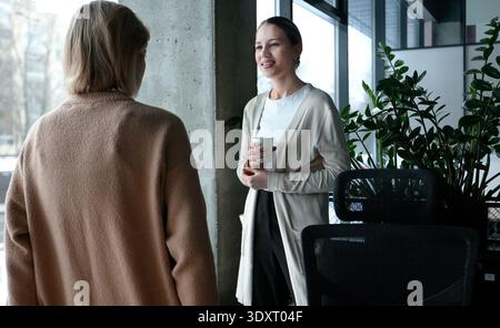 Two women are talking in a room with a potted plant in the background Stock Photo
