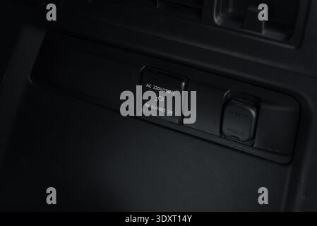 Electrical power outlets in car trunk. Close-up view of a AC 220V power socket with an open cover and a 12V auxiliary power outlet on a dark plastic. Stock Photo