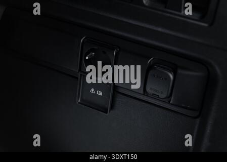 lectric power socket and 12V outlet in car trunk. Close-up view of a Type F AC power socket with an open cover and a 12V auxiliary power outlet. Stock Photo