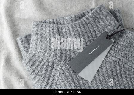 Soft textured sweater of grey luxury natural cashmere with paper tag lying on light wool background. Autumn and winter pure cashmere clothing Stock Photo