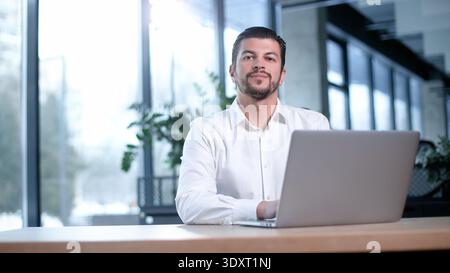 A man is sitting at a desk with a laptop in front of him Stock Photo