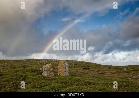 Two limestone boulders in an area of rocky grassland beneath a rainy sky with rainbows in the clouds, Great Orme, Llandudno, North Wales. Stock Photo